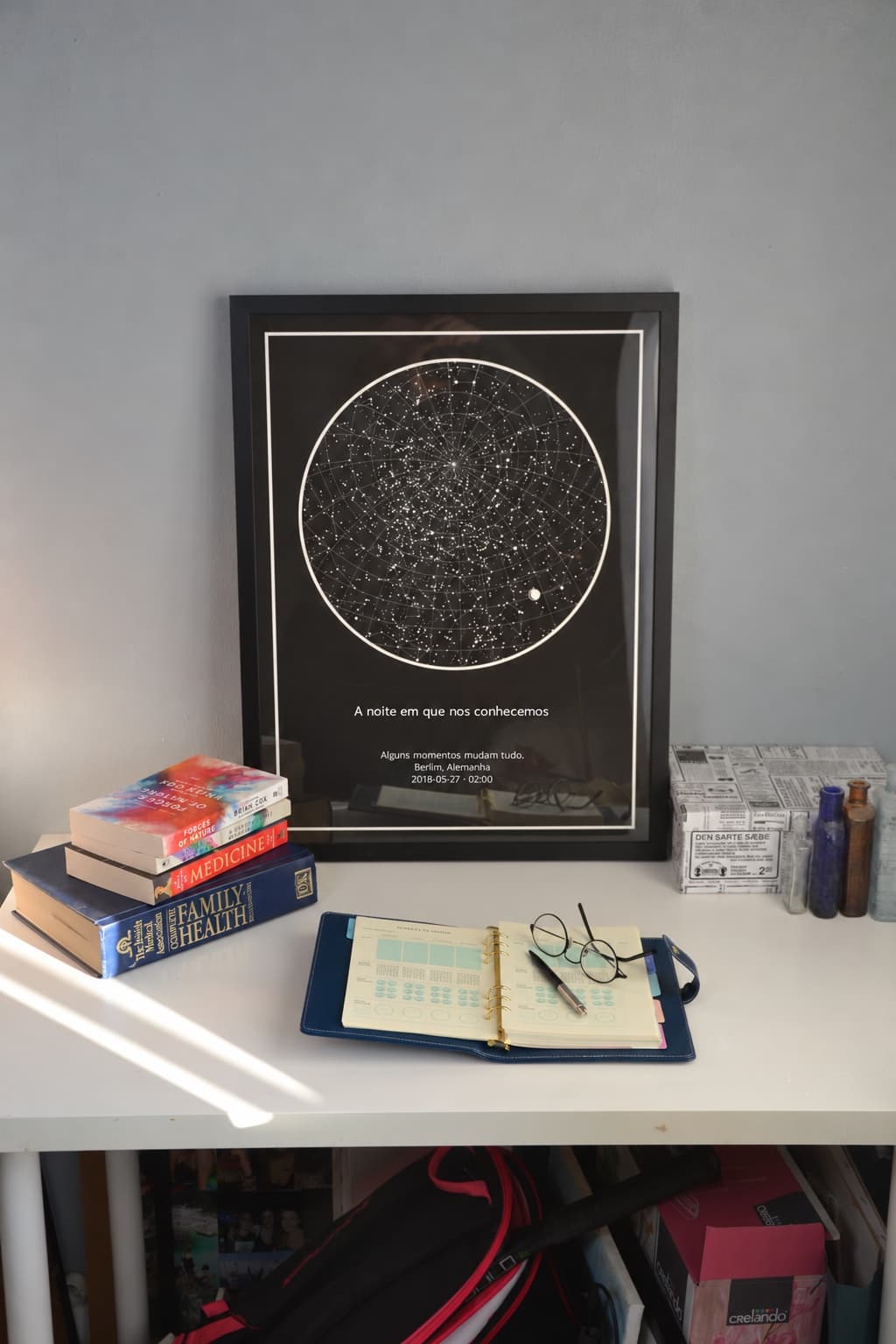 Mapa das estrelas com moldura preta encostado a uma secretária, ao lado de livros e de uma agenda