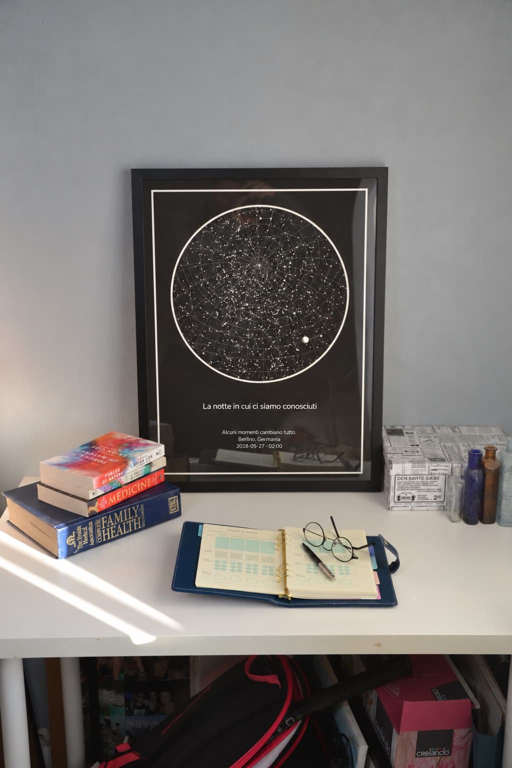 Mappa stellare con cornice nera appoggiata su una scrivania accanto a libri e a un’agenda